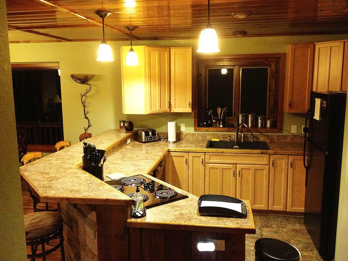 Kitchen with large counter island featuring a stovetop, wood cabinetry, sink, and black refrigerator.