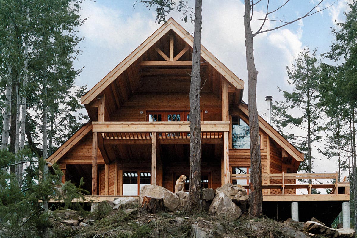 Log home exterior with prominent A-frame gable, exposed rafter tails, two-story covered porch, and multiple windows.