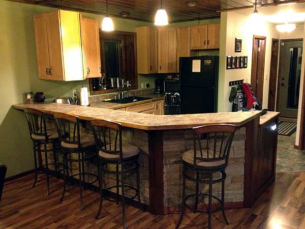 Kitchen bar with stone base and wood cabinetry. Includes sink, refrigerator, and pendant lighting.