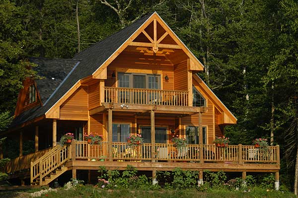 Log home exterior with two balconies, a covered porch, and a prominent gable with decorative timber framing.