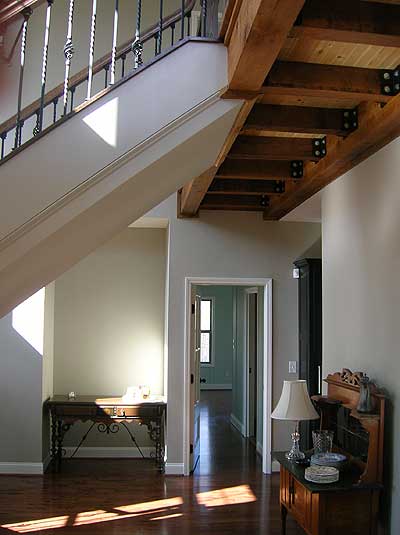 Interior view showcasing a staircase with wrought iron railings, exposed wood beams, and a hallway leading to rooms.