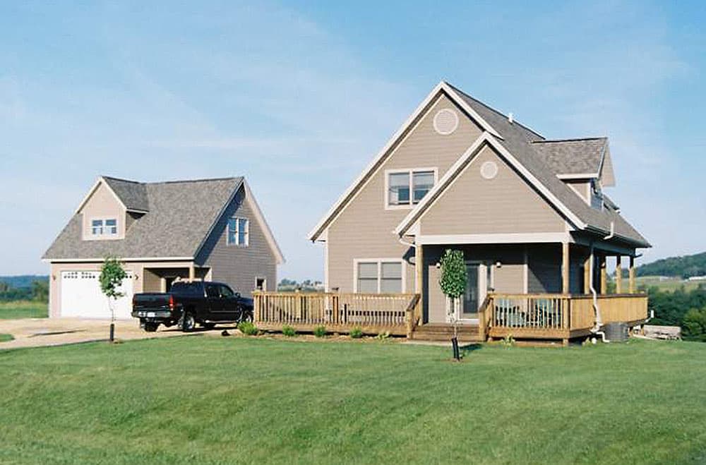 Two-story house plan exterior with gabled dormers, a wrap-around porch with wooden railing, and an attached garage.
