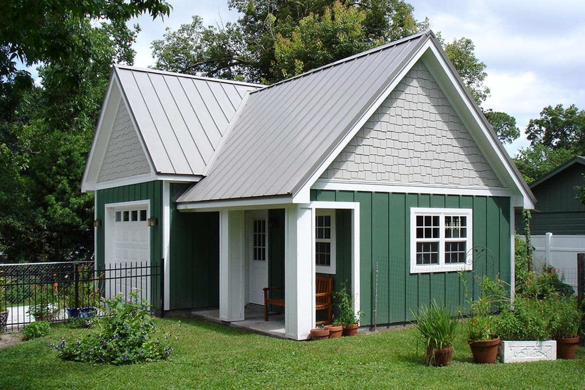 House plan exterior: One-story building with a metal gable roof, vertical siding, shingle gable end, covered porch, and garage door.
