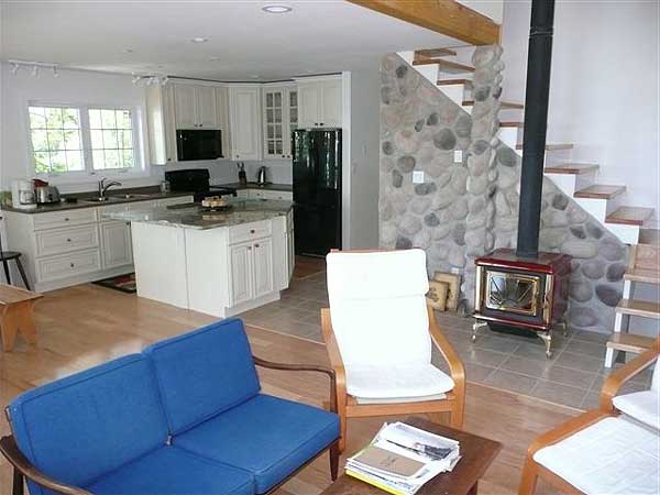 Open concept living area with kitchen island, stone accent wall, wood stove, and stairs.