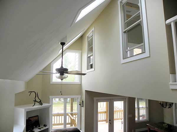 Interior view of a great room with a vaulted ceiling, skylights, ceiling fan, and large windows.
