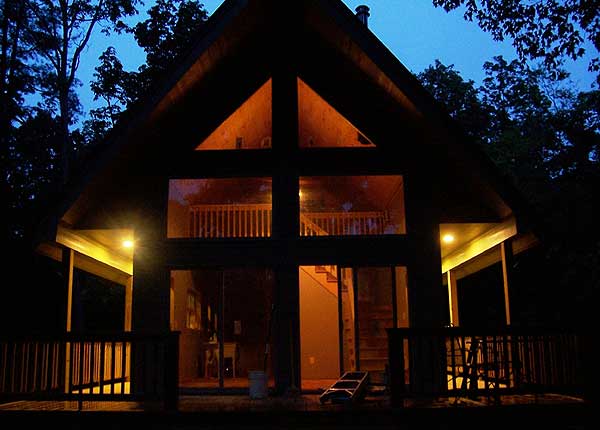House plan exterior with large windows, gabled roof, covered porch, and wood siding at dusk.
