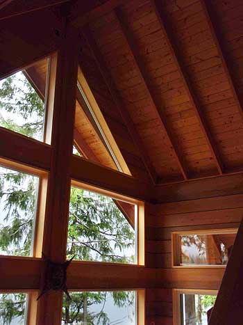 Interior view of a timber-framed room with a vaulted, beamed ceiling and large windows framing trees.